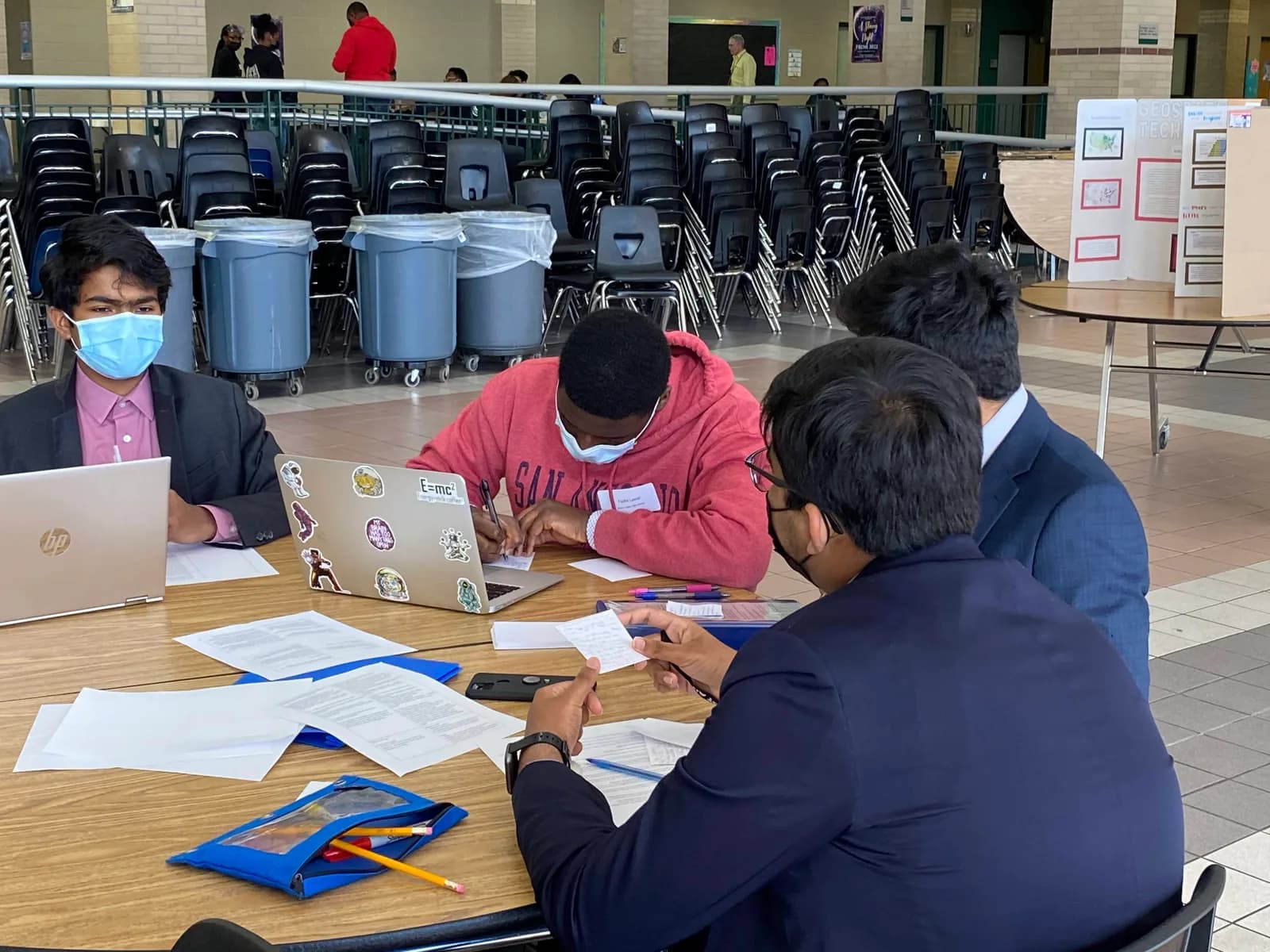 Members reviewing paperwork with laptops at a cafeteria table during Regionals