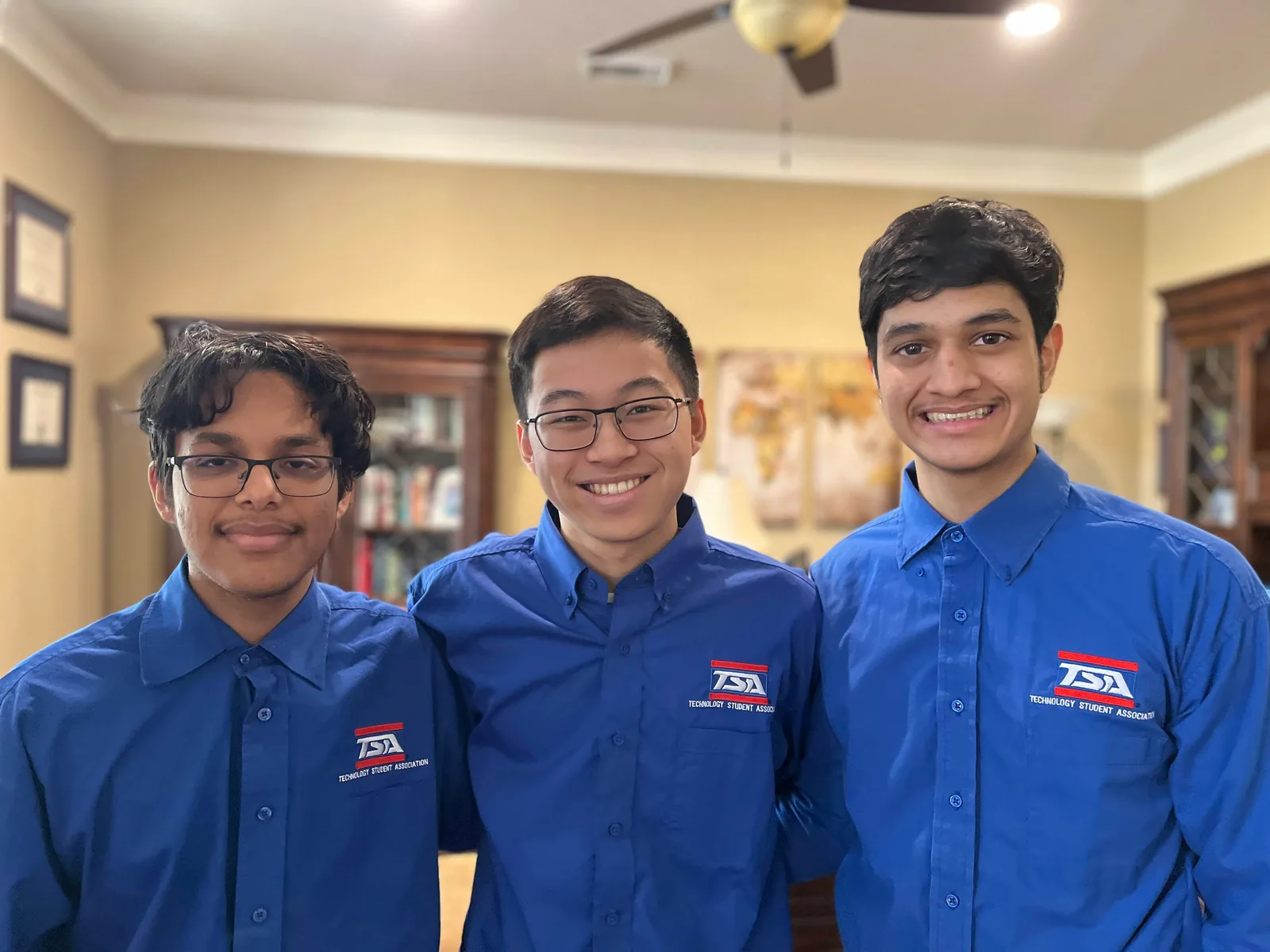 Three members in blue TSA shirts smiling together indoors