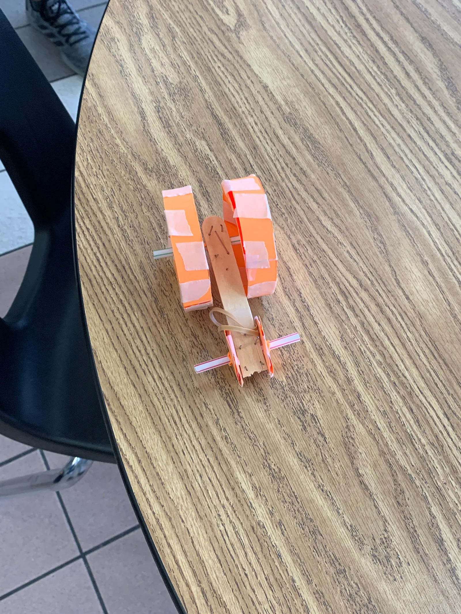 Hand-built orange rubber-band flyer on a cafeteria table