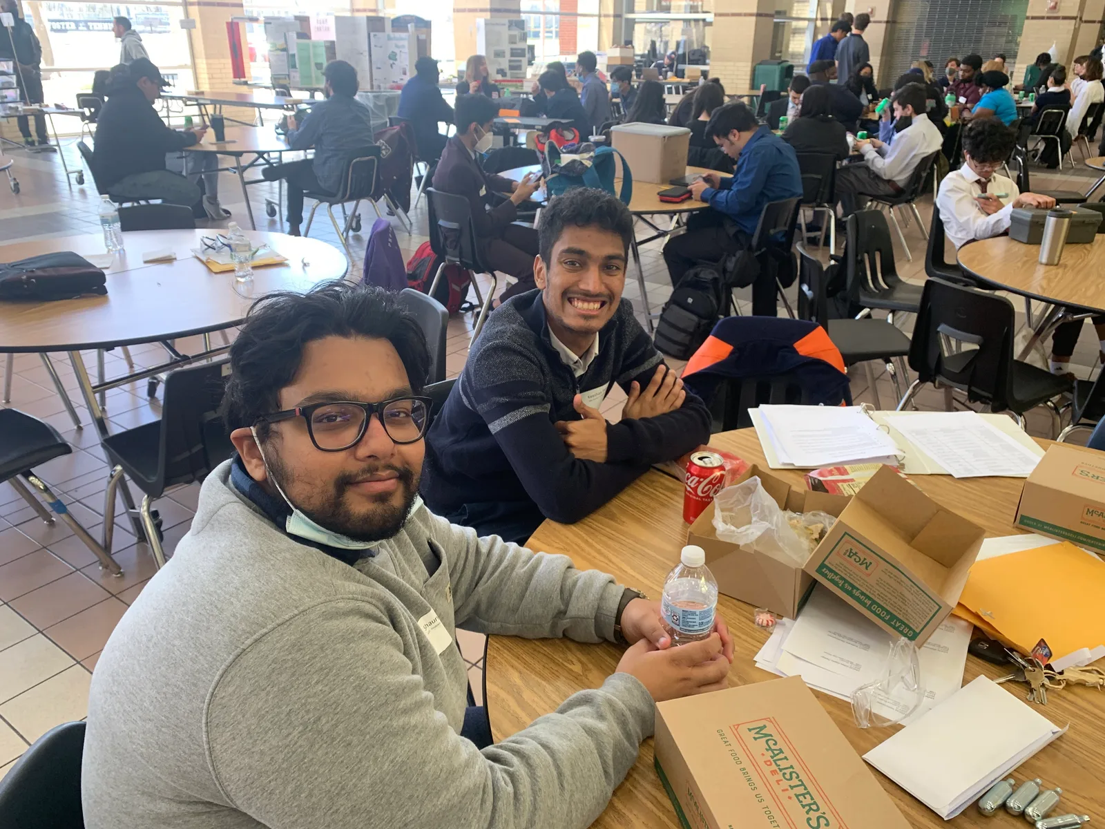 Two members smiling over competition kits and boxes in the cafeteria