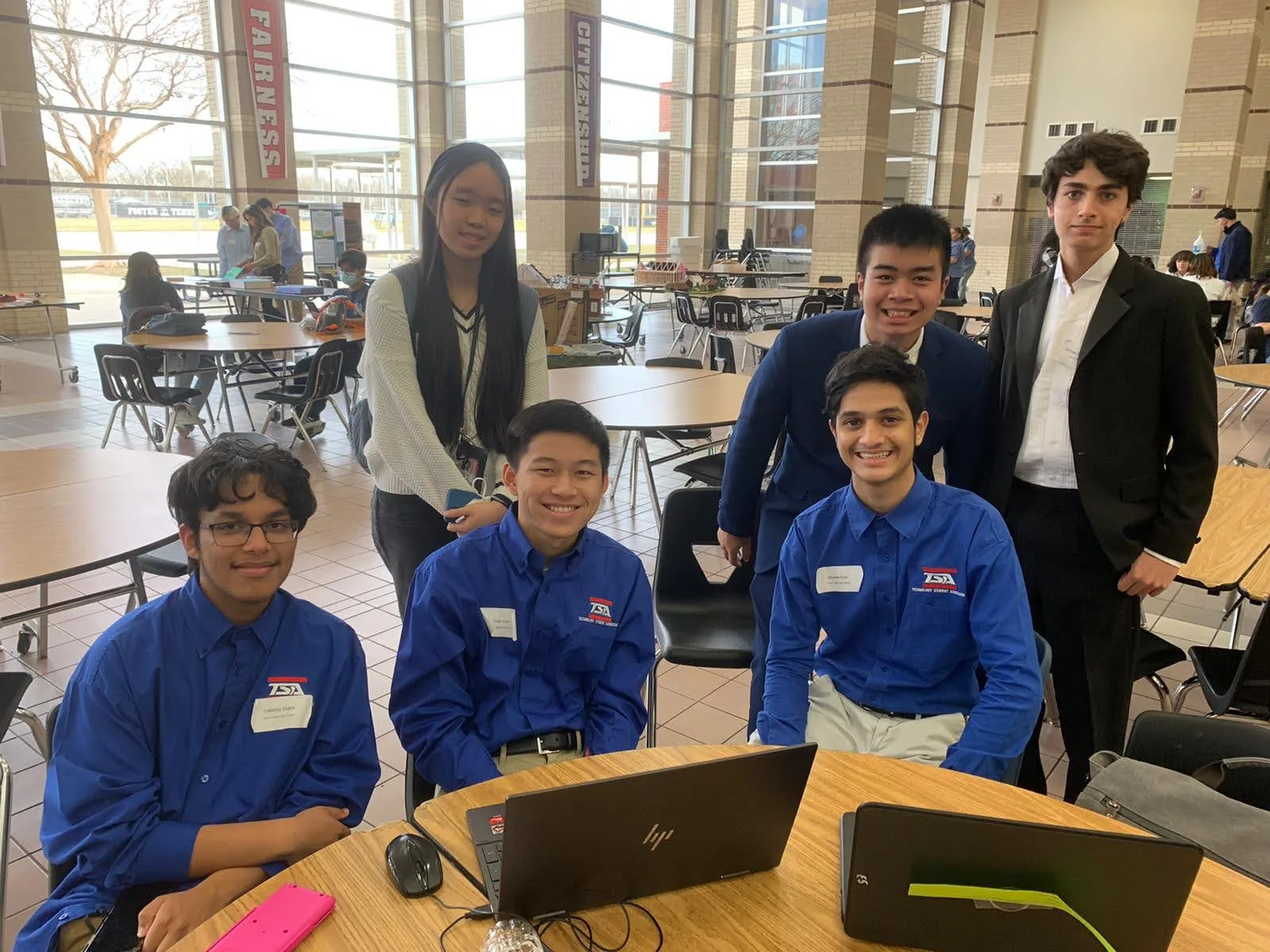 Six members posing together at a work table