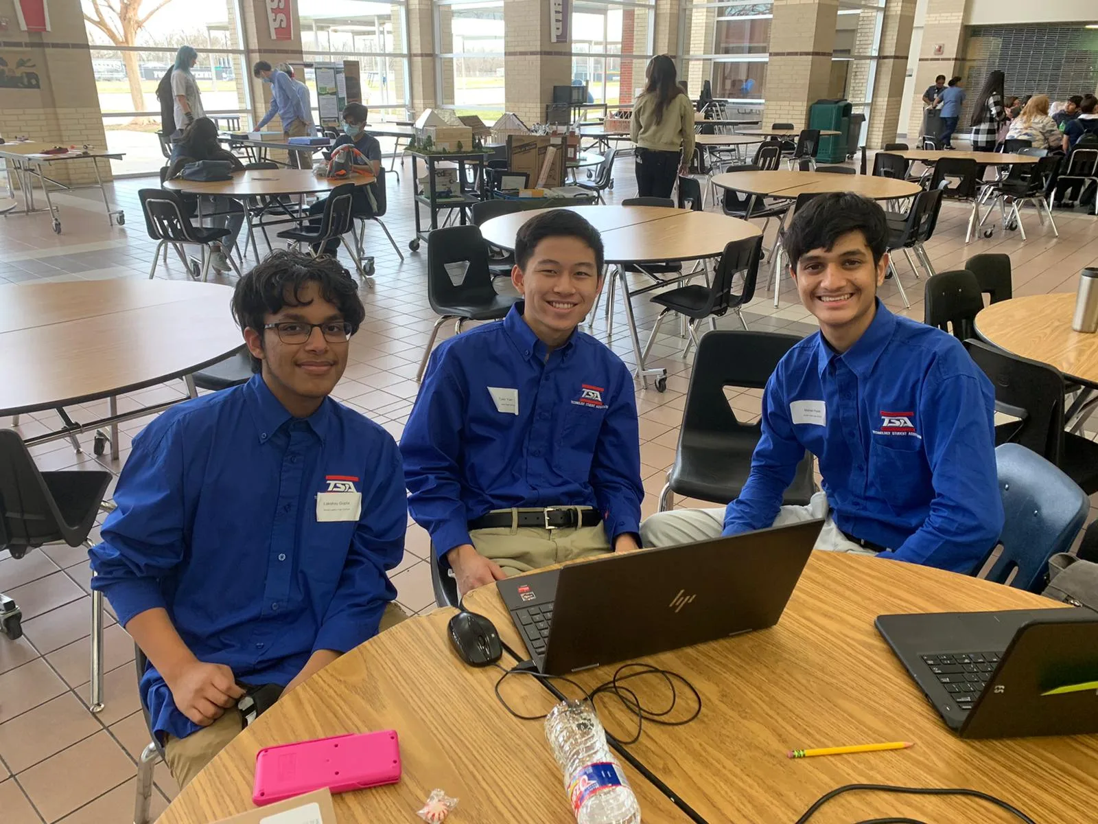 Three members working on laptops at a round cafeteria table