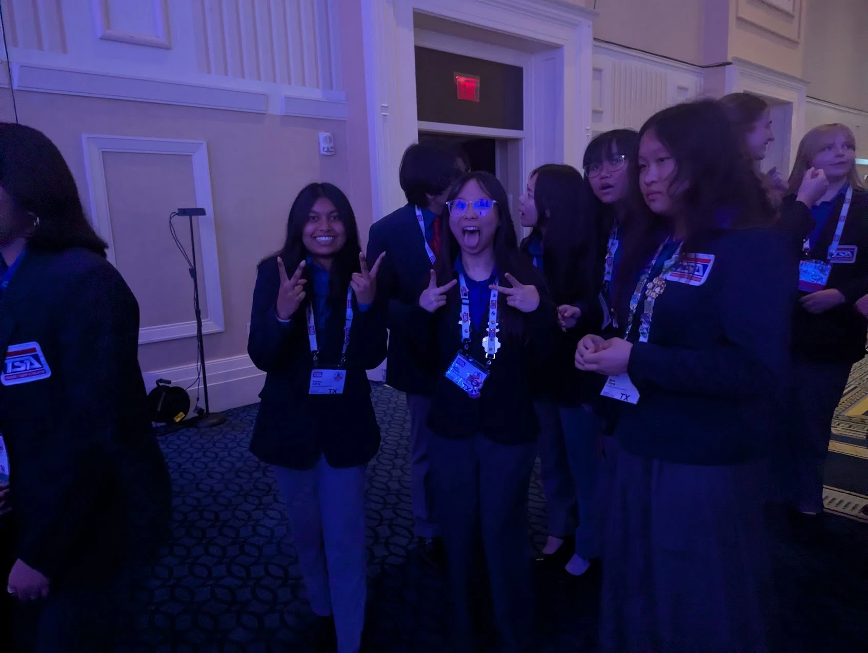 SLHS TSA members in navy competition blazers throwing peace signs in a blue-lit ballroom foyer at the 2026 National TSA Conference
