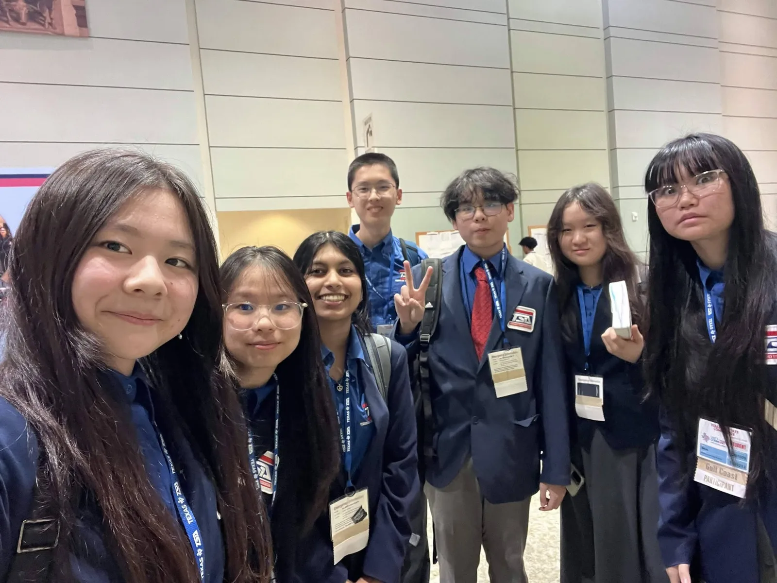 Group selfie of members in navy blazers with blue Texas TSA lanyards and state conference badges inside the convention center