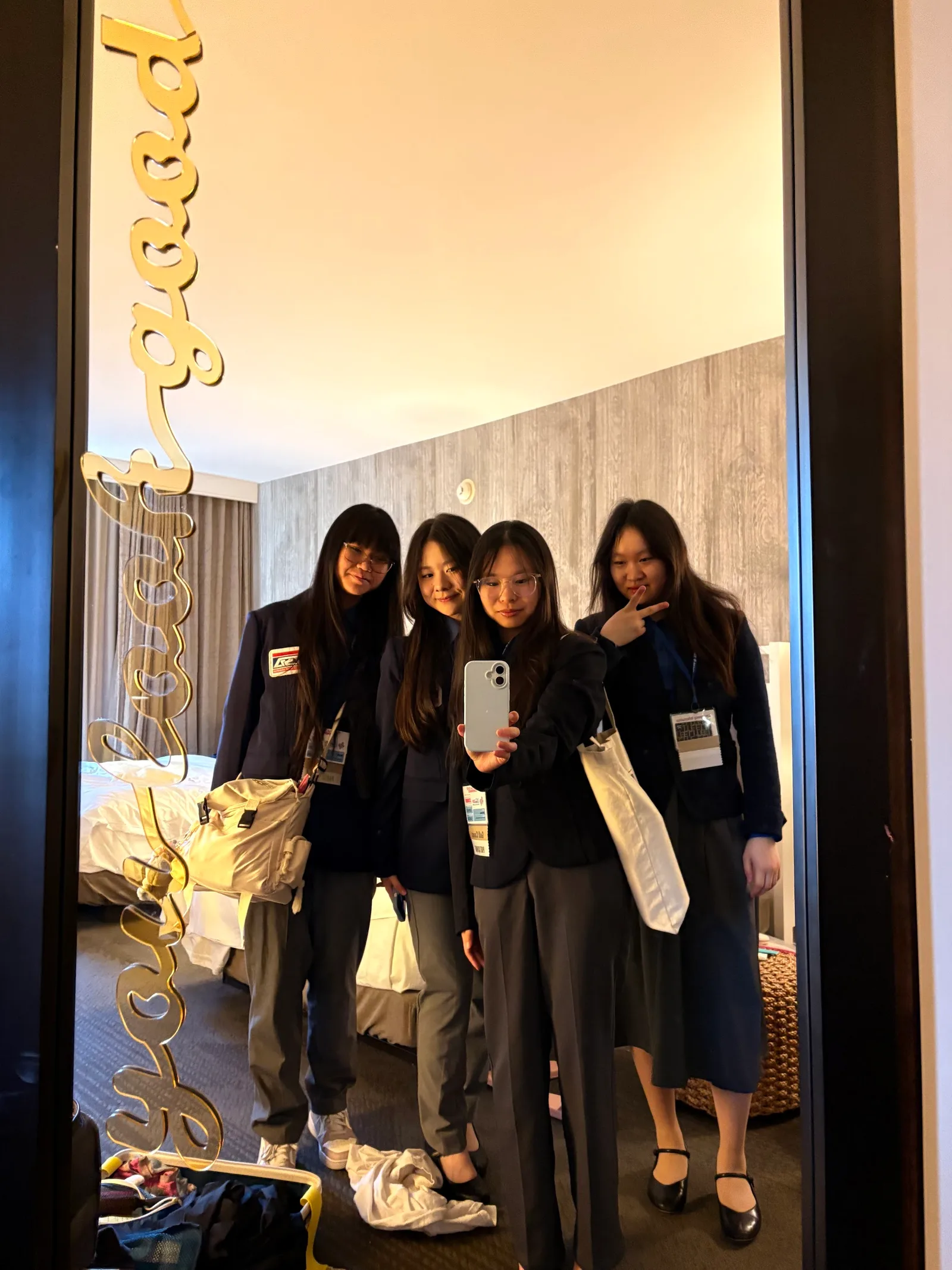 Four members in navy conference blazers with lanyards taking a hotel-room mirror selfie before competition day