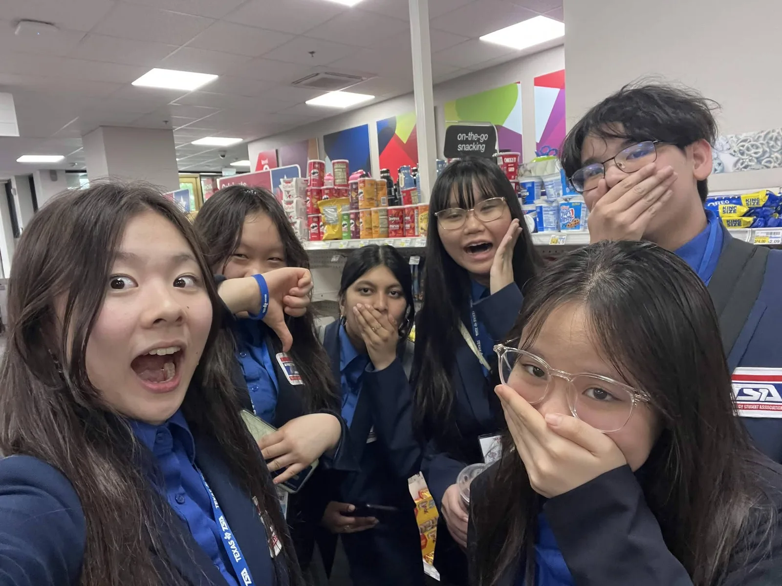 Six members in conference attire making playful faces on a snack run during a break at State
