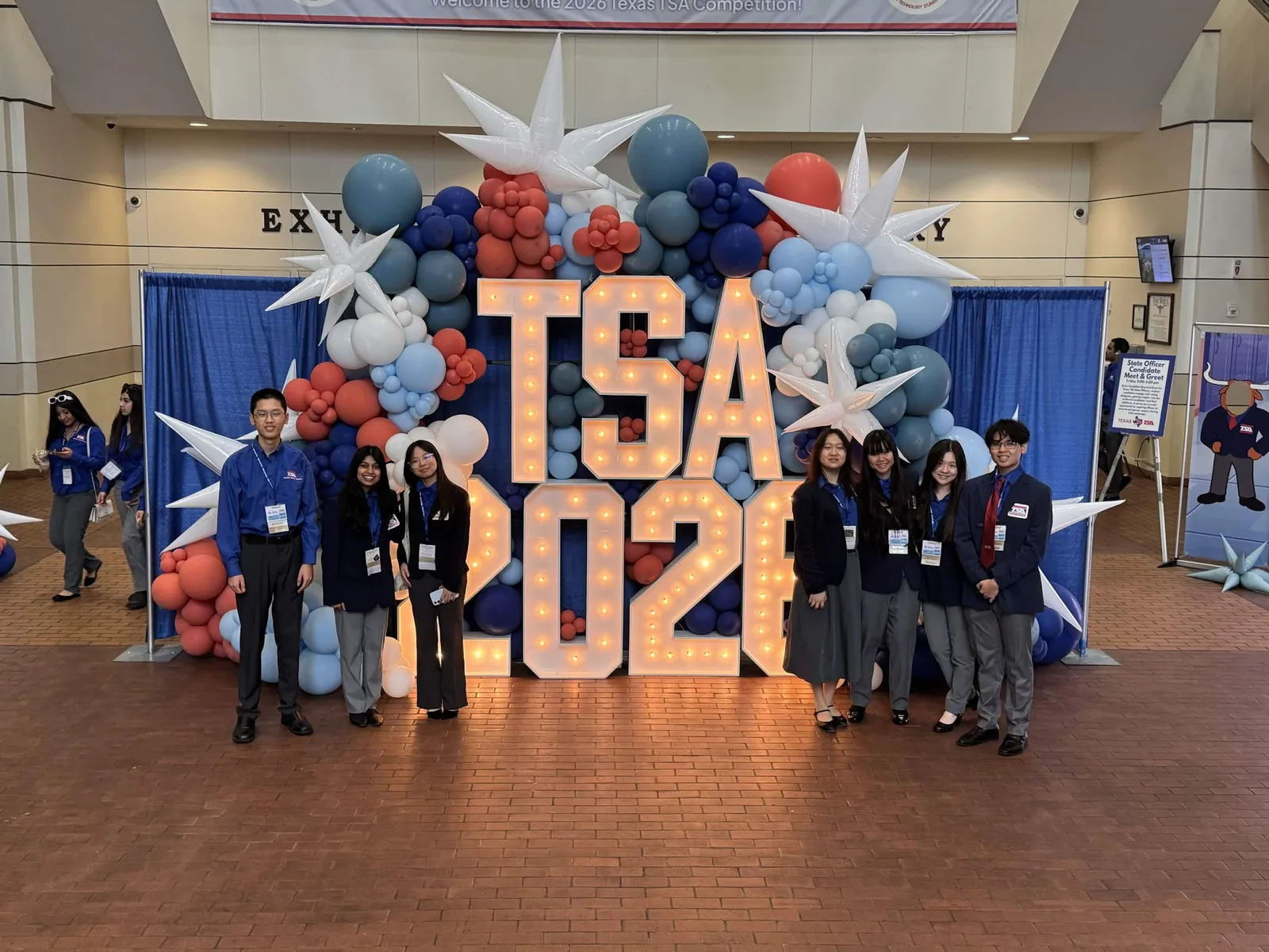 The full SLHS TSA delegation in navy conference blazers posing in front of the giant light-up TSA 2026 marquee letters at the Texas TSA State Conference